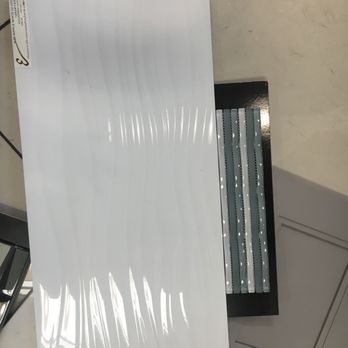 Emser Tile - An alternate choice for the shower tile. - A glossy white tile sample with curved, textured lines is displayed on a black stand, likely in a tile or home improvement store. - Flooring Near Me - Temecula, California