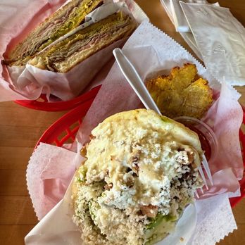 Guava Tree Cafe - Arepa del Patrón - A meal featuring a large sandwich with multiple layers, fried plantain slices, and a salad topped with cheese and dressing, served on a red tray. - Latin American Near Me - Albuquerque, New Mexico