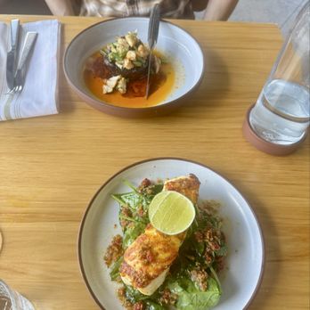 Bulevar Mexican Kitchen - Halibut a la plancha (bottom) and steak (top) - A plate with a grilled fish fillet topped with a lime wedge and greens, and a bowl with a sauce and chopped ingredients, on a wooden table. - Mexican Near Me - Austin, Texas