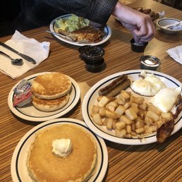 Breakfast Sampler and Grilled Biscuit(bomb) - A breakfast meal with pancakes, hash browns, eggs, sausage, and biscuits is served on plates at a restaurant table.