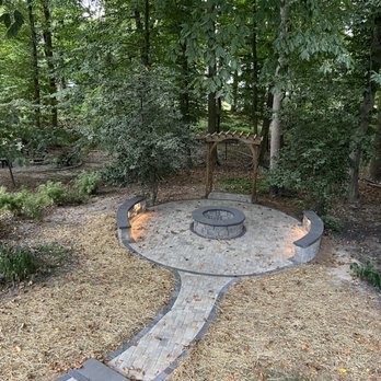 J Imagine Landscaping - a circular fire pit surrounded by trees - Patio Coverings Near Me