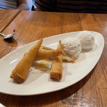 Imm Thai - Fried banana - A dessert plate features fried banana rolls drizzled with honey and two scoops of vanilla ice cream, presented on a white dish. - Thai Near Me - Clark, New Jersey