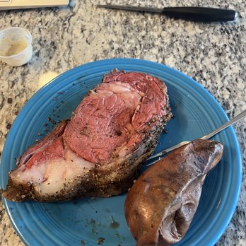 Outback Steakhouse - Supposed to be Seasoned and Seared Prime Rib* - A blue ceramic plate contains a seasoned, cooked prime rib with visible marbling and a beef kidney. The plate is placed on a speckled granite countertop. Nearby, there is a small container of sauce, a knife, a laptop, and a blue mouse pad. The setting appears to be a kitchen or dining area. - Steakhouses Near Me - Dover, Delaware