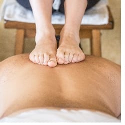 Sore Spots Massage Therapy - Ashiatsu therapy - therapist performs deep tissue pressure point work to the upper back while seated in a high stool.