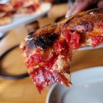 Pie Tap Pizza + Rotisserie + Bar - a hand holding a slice of pizza - Pizza Near Me - Plano, Texas