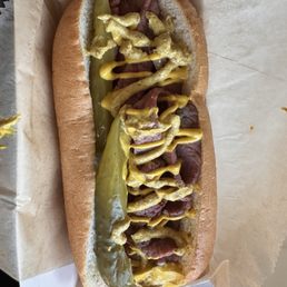 Custom all beef hot dog with pastrami, pickle spears, deli and yellow mustard.