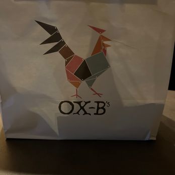 Ox-B’s - Cute takeout bag. Wings were packaged in a box, cornbread in a bag, sides in a cup. - A paper takeout bag features a geometric rooster logo composed of various colored shapes and the text "OX-B's" below it. - Chicken Wings Near Me - Newark, Ohio