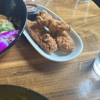 Mixxed DC - Chicken tenders - Fried chicken tenders are placed on a white oval plate, accompanied by a small container of dipping sauce, on a wooden table. - Burgers Near Me - Washington, DC, District of Columbia