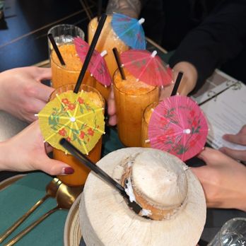 Siam Thai Eatery - Thai ice tea and young coconut - A group of people is sharing drinks with colorful umbrellas and a coconut, likely at a tropical-themed restaurant or bar. - Thai Near Me - Chicago, Illinois