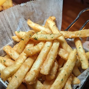 Tavern 157 - Golden French fries with herbs in a metal basket lined with parchment paper, on a wooden table in a restaurant setting. - Lounges Near Me - Flushing, New York