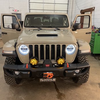 Wildside Customs - Gladiator - A beige Jeep Wrangler with its front doors open, featuring off-road lights, a winch, and a license plate, parked inside a garage with white brick walls. - Auto Customization Near Me - Naperville, Illinois