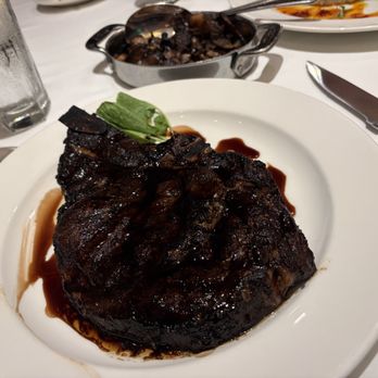 The Capital Grille - Porcini-Rubbed Bone-In Ribeye with 15-Year Aged Balsamic, wild mushrooms in background - Steakhouses Near Me - Tampa, Florida The Capital Grille - Porcini-Rubbed Bone-In Ribeye with 15-Year Aged Balsamic, wild mushrooms in background - Steakhouses Near Me - Tampa, Florida
