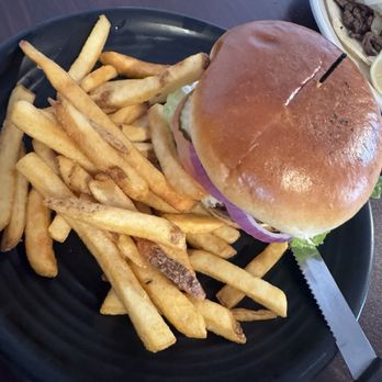 Rock Reef Cafe - A cheeseburger with lettuce, tomato, and onions on a bun, served with a side of French fries on a black plate. - Pizza Near Me - Torrey, Utah