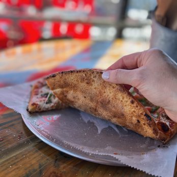 Red Tractor Pizza - a hand holding a piece of pizza - Pizza Near Me - Bozeman, Montana