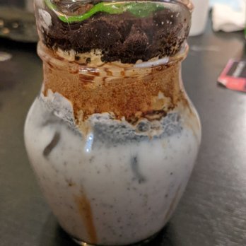 Unicorn Cafe - Front view of my black sesame potted plant - A dessert in a small glass jar features layers of cookies, cream, and chocolate, topped with mint leaves. - Themed Cafes Near Me - Toronto, Ontario