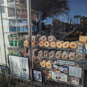 Barrio Bread - Bagels in the WIndow almost to the front - Bakery storefront window showing bagels, bread, and bakery products, with newspaper clippings and awards displayed at the bottom. - Bakeries Near Me - Tucson, Arizona