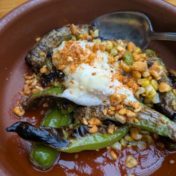 Pilsen Yards - Roasted Shishito peppers - A dish of roasted shishito peppers with toppings like sour cream and crunchy bits, served in a brown bowl with a metal spoon. - Tacos Near Me - Chicago, Illinois
