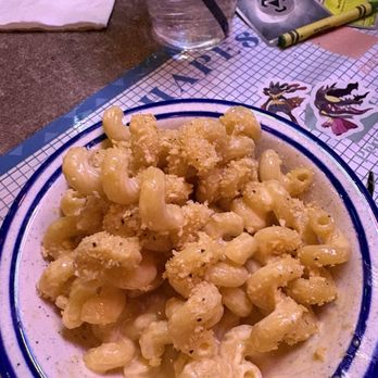ODB's Classy Dive - Side Mac and cheese - A close-up of a bowl of macaroni and cheese topped with breadcrumbs, served on a restaurant table. The table has a glass of water, a notebook, a pen, and some decorative items. The setting suggests a casual dining environment. - Cocktail Bars Near Me - West Allis, Wisconsin
