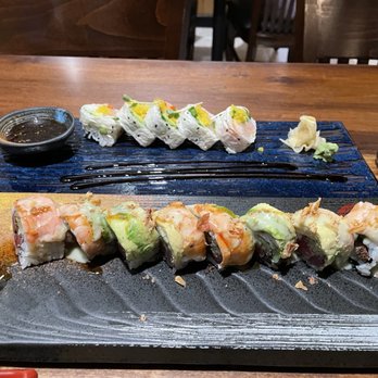 Komeya - Zero Sen roll in the back and the Golden Hill Roll in the front. Beautiful presentation!! - Assorted sushi rolls with toppings like shrimp and avocado are presented on black and blue plates, accompanied by soy sauce, wasabi, and ginger. - Sushi Bars Near Me - Spring, Texas