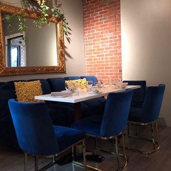 Mint - Blue room - A dining table with blue velvet chairs and yellow pillows is set with glassware and napkins in a restaurant with a brick wall and a large ornate mirror. - Cocktail Bars Near Me - Glens Falls, New York