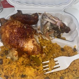 This is the Rotisserie Chicken w/ yellow rice   "Muy enamorada" - A takeout container contains a serving of rotisserie chicken with crispy skin placed on yellow rice mixed with beans. There are also pieces of cooked chicken meat in a separate section of the container. A white plastic fork is included in the container, and the meal appears to be from a Dominican restaurant offering seasoned dishes.