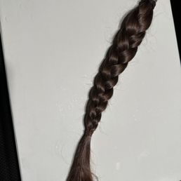 12-inches of 'virgin hair' ready for donation to  Locks of Love - A single braid of brown hair is positioned on a white surface, with the hair tied at the end. The braid appears to be freshly cut, with some loose strands at the end. The surface is plain and unadorned, providing a clear view of the hair's texture and color.
