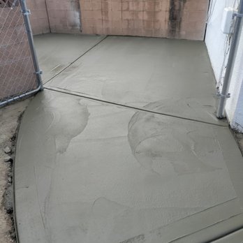 FullShield - More of the new work, done in 1 day by 3 men - Concrete has been recently poured and smoothed in a small outdoor yard, with a chain-link gate on the left and a brick wall at the back. - Insulation Installation Near Me