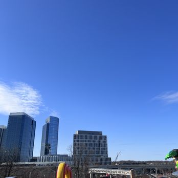 Shipgarten - The image features a city skyline with multiple modern high-rise buildings, including glass-covered towers, set against a clear blue sky. In the foreground, there is a colorful inflatable playground with red, yellow, green, and blue sections, indicating a recreational area possibly near a park or family-friendly venue. - Beer Gardens Near Me - Mclean, Virginia