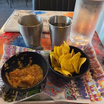 Tiki Bird - Plantain chips and Caribbean salsa with metal cups with Coconut Old Fashioned on left and water on right - Wine Bars Near Me - Grand Junction, Colorado Tiki Bird - Plantain chips and Caribbean salsa with metal cups with Coconut Old Fashioned on left and water on right - Wine Bars Near Me - Grand Junction, Colorado