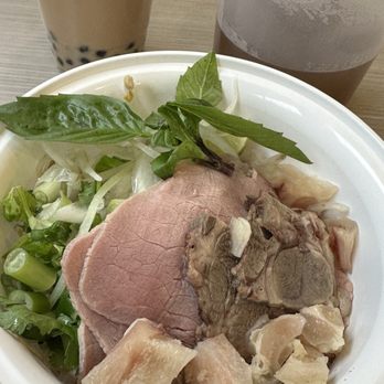 Hanco’s - Beef Broth Pho - A bowl of Vietnamese beef pho with herbs, vegetables, and chunks of meat, served with bubble tea and iced coffee in the background. - Vietnamese Near Me - Brooklyn, New York