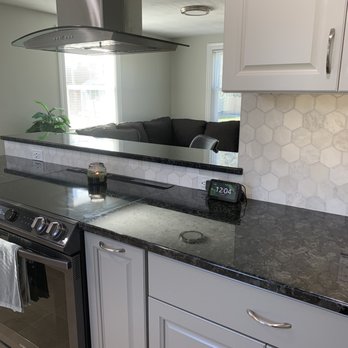Pro Finish Carpentry & Remodeling - a kitchen with white cabinets and black countertops - General Contractors Near Me