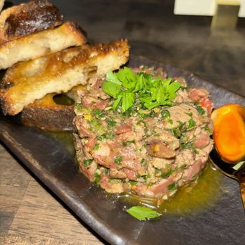 Pretty Penny - Beef tartare - Beef tartare served with toasted bread and a cherry tomato on a dark plate, garnished with fresh herbs, in a restaurant setting. - Cocktail Bars Near Me - Phoenix, Arizona