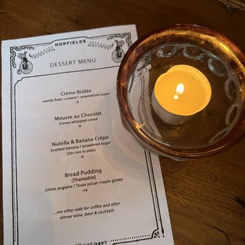 Hopfields - dessert menu - we were too full but it looked great - A dessert menu from Hopfields restaurant is placed on a wooden table, accompanied by a lit candle in a glass holder. - Pubs Near Me - Austin, Texas