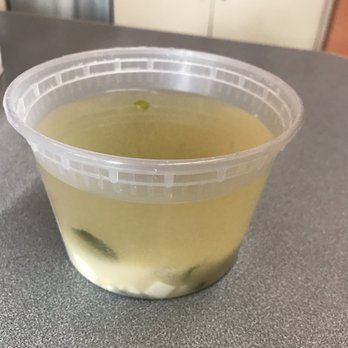 Osaka - Soup with sushi rolls. - A transparent plastic cup containing a pale yellow-green liquid with some solid pieces at the bottom, placed on a gray surface. - Japanese Near Me - Pawtucket, Rhode Island