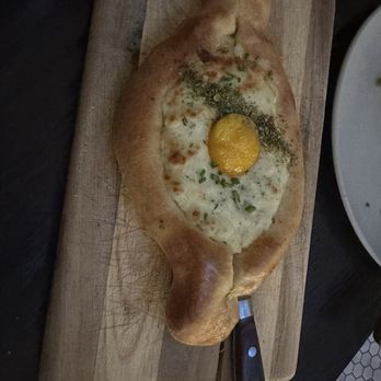 Sudova * Eastern European Kitchen - Cheese bread - A bread shaped like a chicken with an egg yolk on top, garnished with herbs, placed on a wooden serving board. - Modern European Near Me - Cincinnati, Ohio