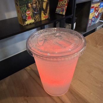 THC by Chitiva - South Loop - A pink, translucent drink in a clear plastic cup with a lid, placed on a wooden table in a game store or lounge setting. - Vitamins & Supplements Near Me - Chicago, Illinois