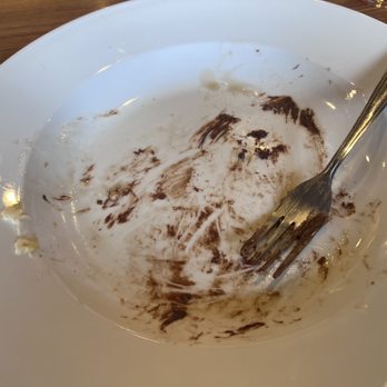 Denny's - Finished plate - A white dessert plate with leftover chocolate sauce and crumbs, accompanied by a metal fork, on a wooden table. - Breakfast & Brunch Near Me - Waldorf, Maryland