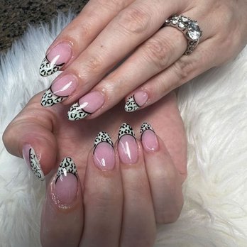 Bruce Nails - Hands with manicured nails displaying a leopard print design on the tips, wearing a silver ring with gemstones, resting on a soft, white surface. - Nail Salons Near Me - Burlington, Massachusetts