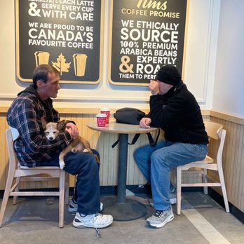 Tim Hortons - two men sitting at a table with a dog - Coffee & Tea Near Me - Toronto, Ontario