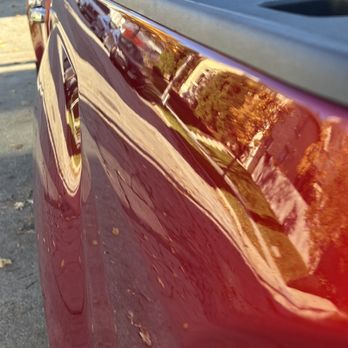 Acci-Dent - Fixed - The image captures the side of a red vehicle with a reflective surface, showing reflections of nearby buildings, trees, and the sky. - Auto Repair Near Me - Glendale, Wisconsin