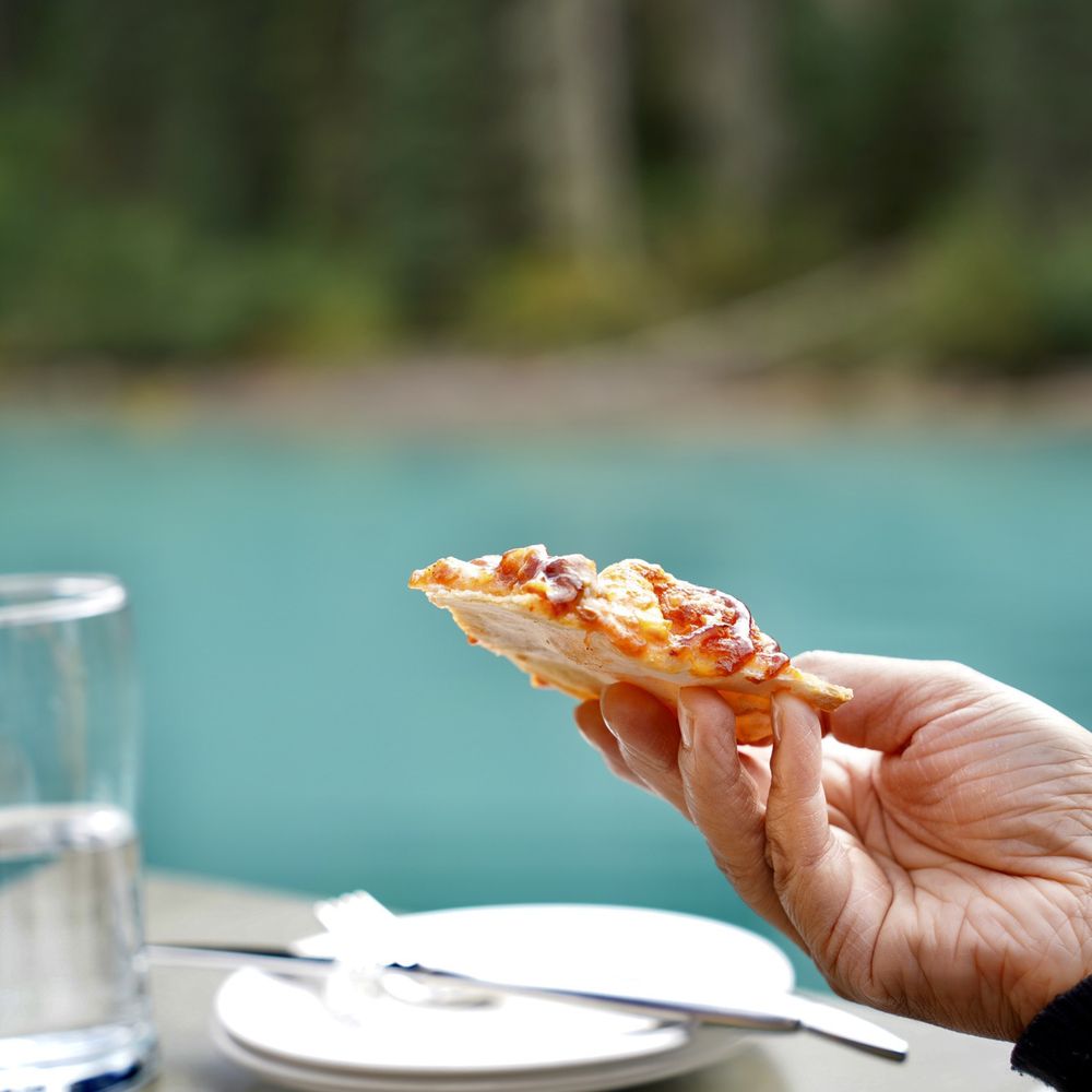 Cilantro on the Lake - a hand holding a slice of pizza - Canadian (New) Near Me - Field, British Columbia