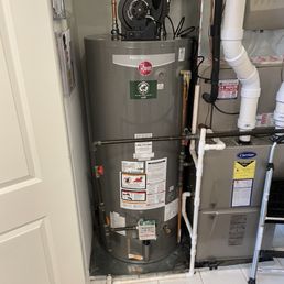 New Rheem water heater installed - A Rheem water heater is situated in a small utility space, connected to plumbing and electrical systems, with labels and safety instructions visible.