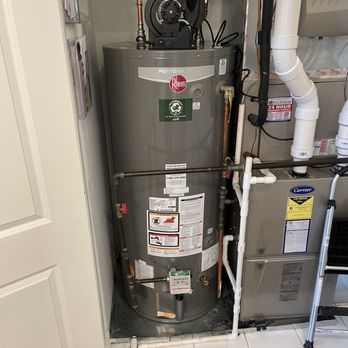 Fast Plumbing 247 - New Rheem water heater installed - A Rheem water heater is situated in a small utility space, connected to plumbing and electrical systems, with labels and safety instructions visible. - Water Heater Installation/Repair Near Me