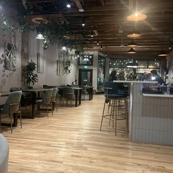 Method & Muse Spirits - Inside - A cafe interior featuring wooden flooring, various seating options, hanging pendant lights, and decorative plants along the walls. - Distilleries Near Me - Arvada, Colorado