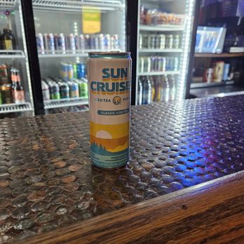 Mike's Grill - A Sun Cruise iced tea can is on a textured bar counter with refrigerators and drinks in the background. - Dive Bars Near Me - Columbus, Ohio