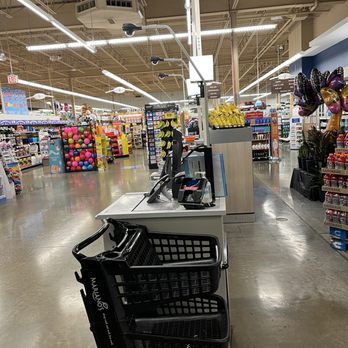 Mariano's - The self checkout bays at 7am this morning after my purchase! AWOL employees gossip 100 feet away! - Checkout station with a black shopping cart positioned in front of a cash register and payment terminal. The store aisle features shelves stocked with various products, including balloons, snacks, and toys. Bright overhead lighting illuminates the space, and the ceiling reveals exposed pipes and ductwork. The scene captures a typical grocery store environment with organized product displays and a clean, polished concrete floor. - Grocery Near Me - Westchester, Illinois