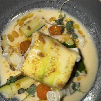 Harbinger - Halibut wrapped in zucchini. - A seafood dish with halibut wrapped in zucchini, served with a creamy sauce, cherry tomatoes, microgreens, and decorative elements. - New American Near Me - Des Moines, Iowa