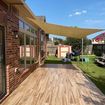 Salgado Construction - Patio - A backyard patio area features a beige shade sail, brick house with large windows, and a wooden fence enclosing the yard. - General Contractors Near Me - Channelview, Texas