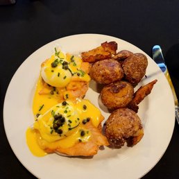 Classic Eggs Benedict - Poached eggs topped with hollandaise sauce and chives, accompanied by roasted potatoes on a white plate.