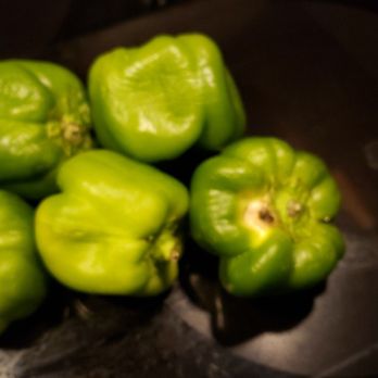 Produce Junction - Wilted green peppers and mold - Five green bell peppers are arranged on a dark surface, with some showing minor blemishes and uneven coloring. - Fruits & Veggies Near Me - Exton, Pennsylvania